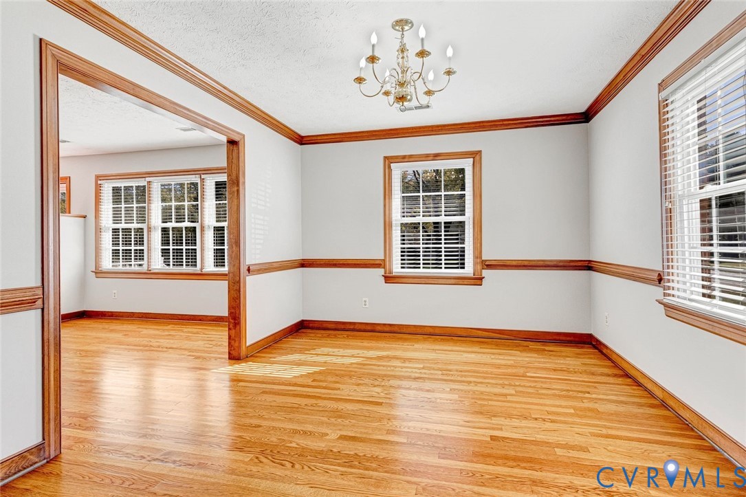 Room featuring wood-finish flooring, multi-pane windows with horizontal blinds, decorative chair rail molding, ceiling-mounted chandelier, and wood-finish door casing