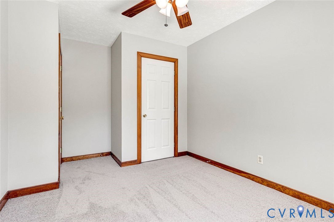 Room featuring neutral-toned carpeting, wood-finished trim, a six-panel door, and a ceiling-mounted fan with light fixture