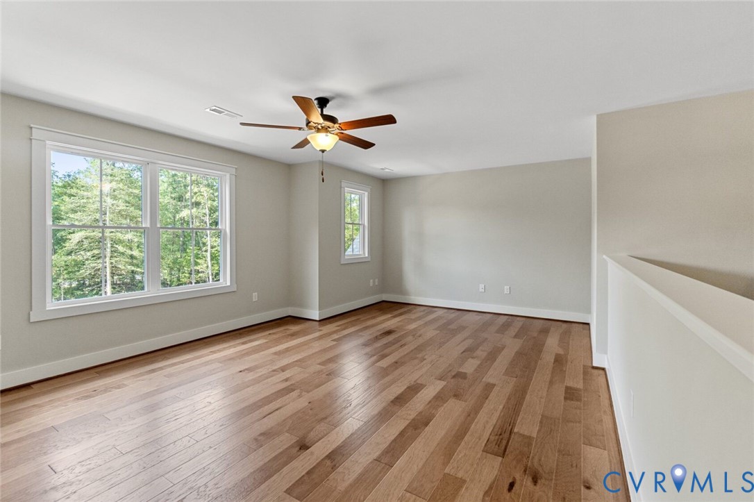 Spacious room featuring wood-finish flooring, multi-pane windows, a ceiling fan with light fixture, and neutral wall tones