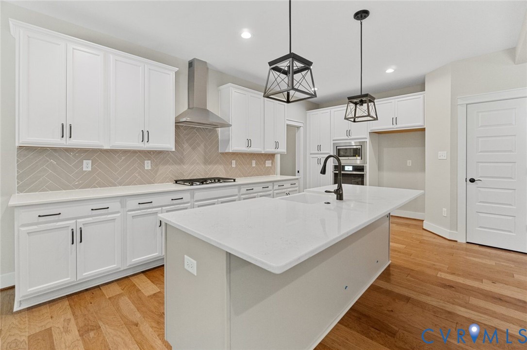 Kitchen featuring white cabinetry, center island with stone countertop, herringbone-patterned backsplash, stainless steel range hood, and wood-finish flooring