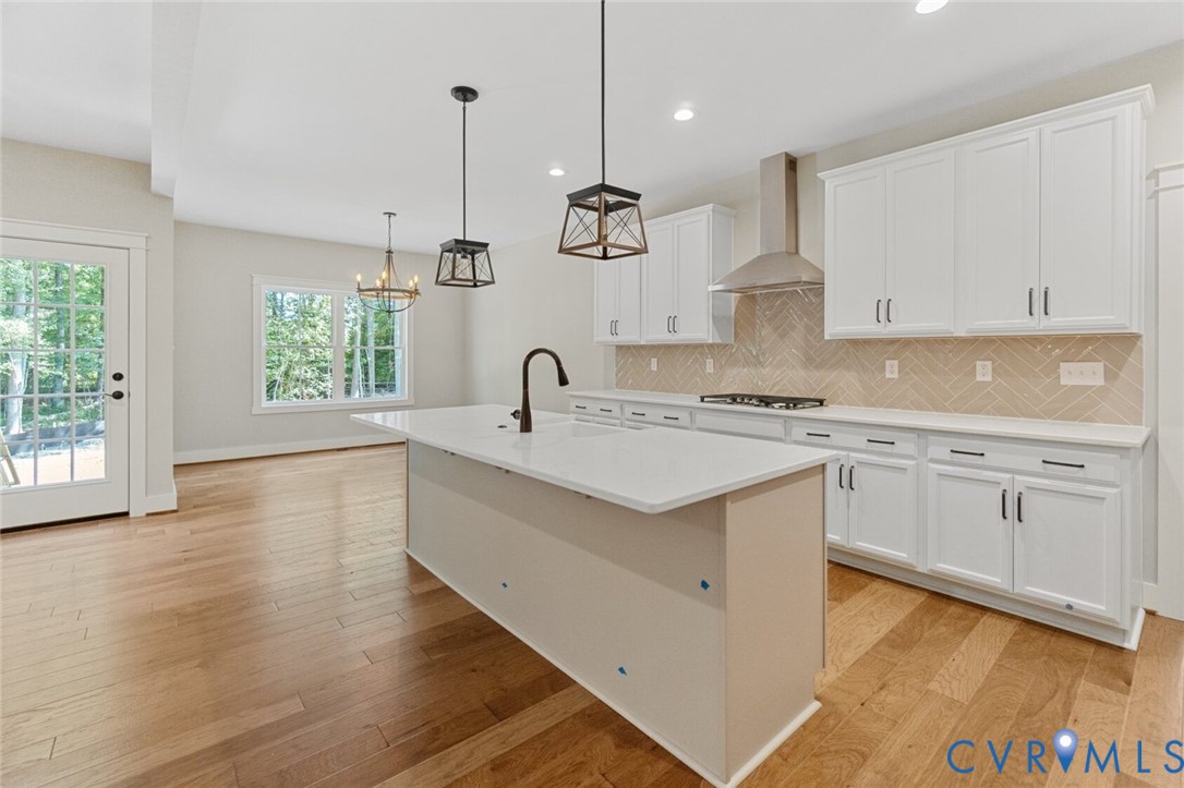 Kitchen featuring white shaker-style cabinetry, quartz countertops, a central island with a matte black faucet, herringbone-patterned tile backsplash, and wood-finish flooring