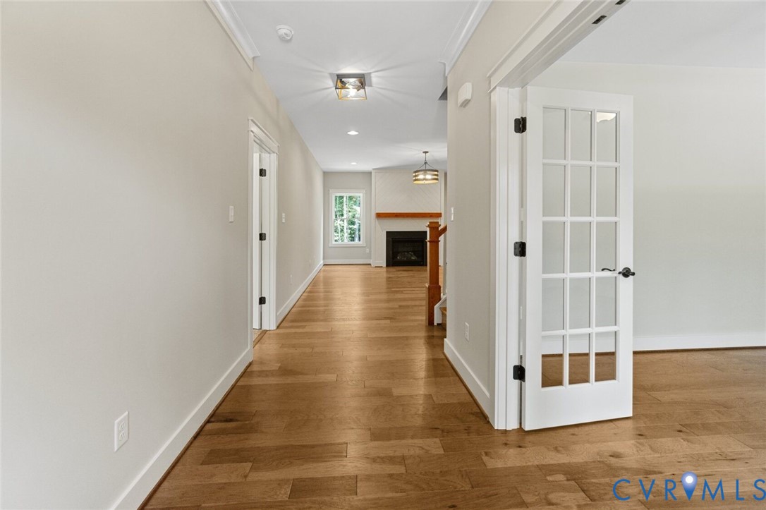 Interior hall featuring wood-finish flooring, white French doors with glass panes, crown molding, recessed lighting, and a fireplace with a wood mantel Interior hall featuring wood-finish flooring, white French doors with glass panes, crown molding, recessed lighting, and a fireplace with a wood mantel