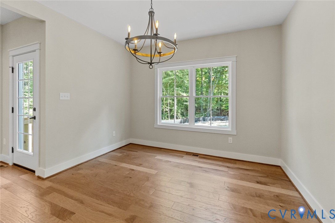 Neutral-toned interior featuring wood-finish flooring, a multi-light metal chandelier, a large double-hung window, and a glass-paneled exterior door