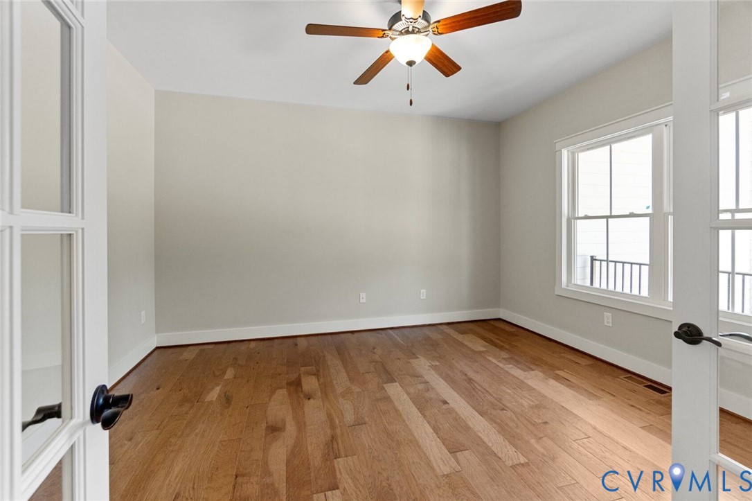 Interior space featuring wood-finish flooring, double glass-paneled doors, multi-pane windows, and a central ceiling fan with an integrated light fixture Interior space featuring wood-finish flooring, double glass-paneled doors, multi-pane windows, and a central ceiling fan with an integrated light fixture