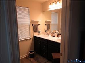 Bathroom featuring dark-finished cabinetry, solid-surface countertop with integrated sinks, full-width vanity mirror, and multi-bulb over-mirror lighting