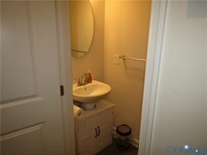White cabinet vanity with a pedestal-style sink, oval wall-mounted mirror, and metallic hardware finish