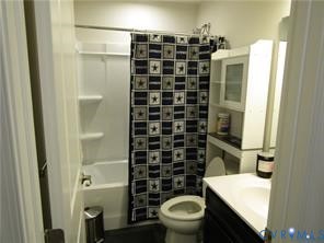 Bathroom featuring an integrated tub and shower unit, built-in shelving, and a vanity cabinet with a light-toned countertop