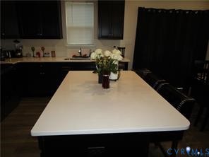 Kitchen island with a solid-surface countertop and dark-finish cabinetry, complemented by dark-finish upper and lower cabinetry, and wood-finish flooring