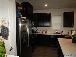 Kitchen featuring dark cabinetry, stainless steel refrigerator, light-toned countertops, and wood-finish flooring