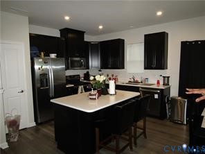 Kitchen featuring dark cabinetry, quartz countertops, a center island with integrated seating, stainless steel appliances, and wood-finish flooring