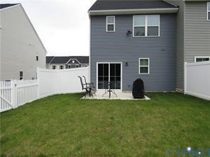Rear exterior featuring horizontal vinyl siding, a concrete patio, and a white privacy fence enclosing the grass lawn