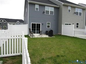 Rear exterior featuring lap siding, concrete patio, and white vinyl privacy fencing enclosing a grass lawn