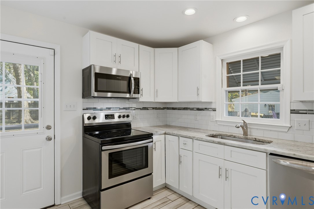 Kitchen featuring white shaker-style cabinetry, stone-finish countertops, stainless steel appliances, subway tile backsplash with decorative inset