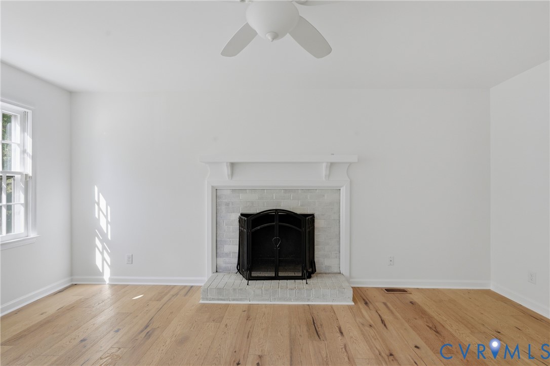 Fireplace featuring a light-toned brick surround, raised hearth, and mantel, complemented by wood-finish flooring and a ceiling-mounted fan