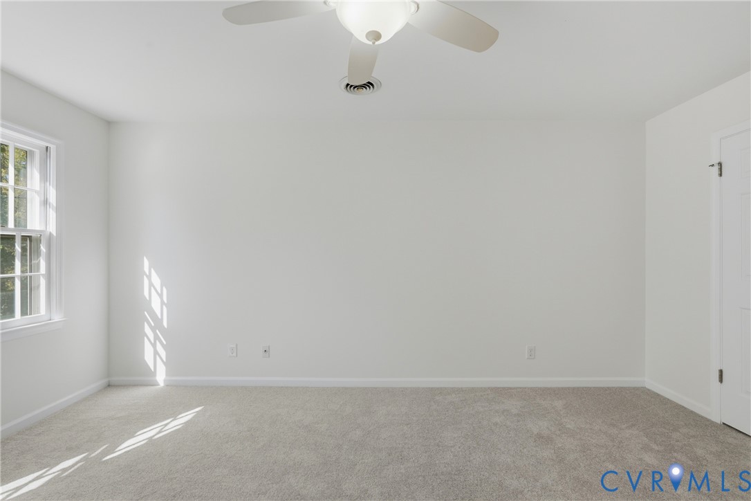 Neutral-toned carpeting, multi-pane window, white-finish door, and ceiling-mounted light fixture with fan