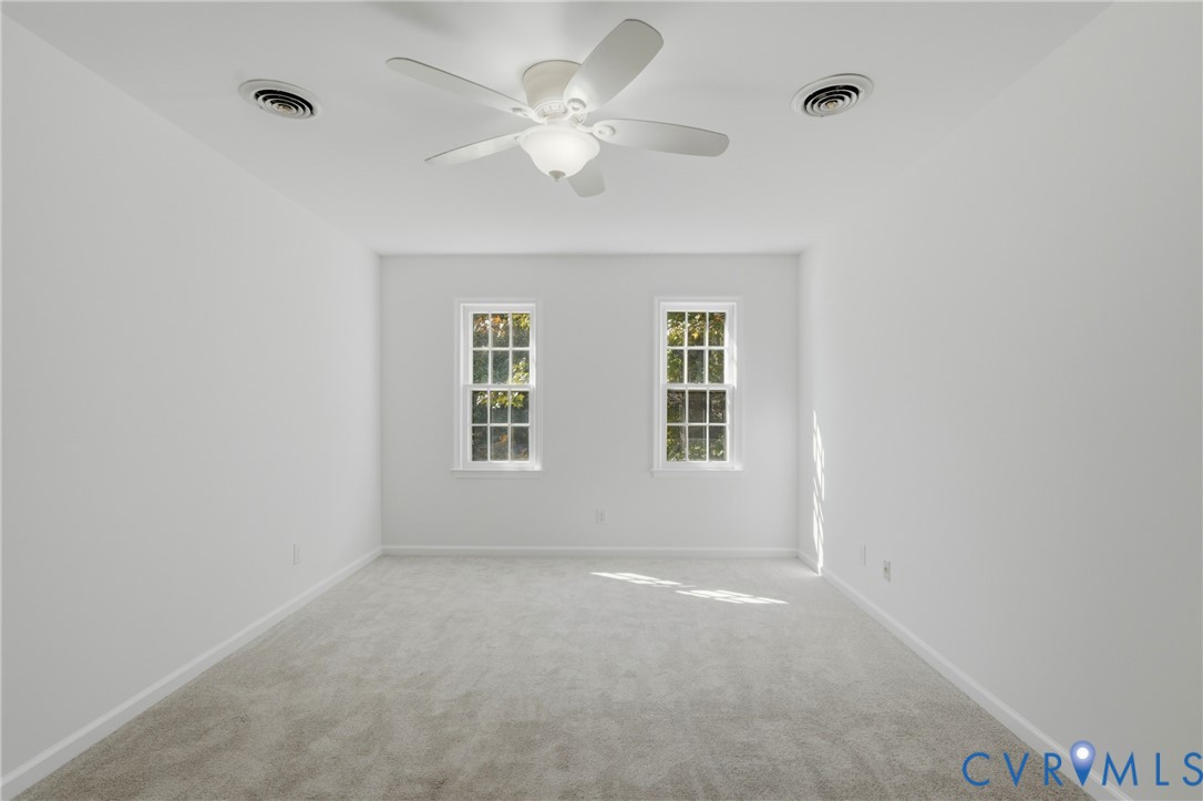 Neutral-toned carpeting, multi-pane windows, and a ceiling-mounted fan with integrated light fixture