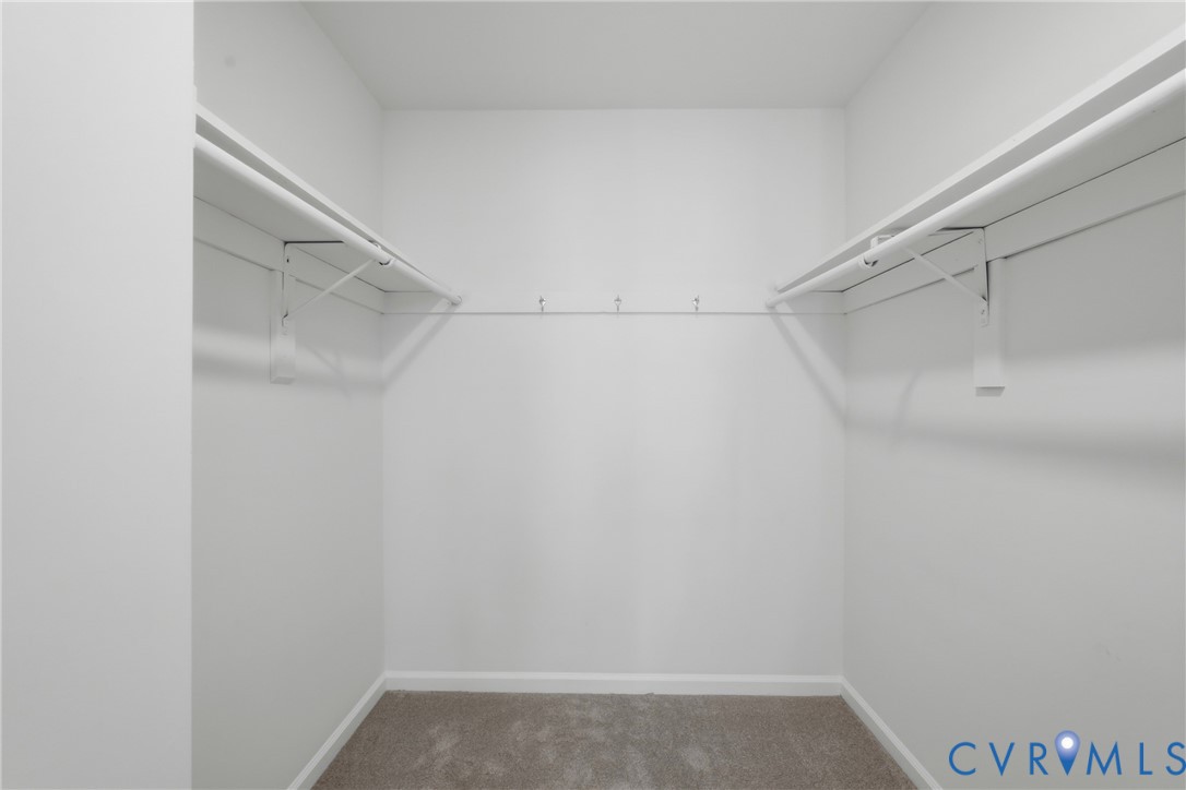 Walk-in closet featuring neutral carpeted flooring, white walls, and dual-level built-in shelving with integrated garment rods