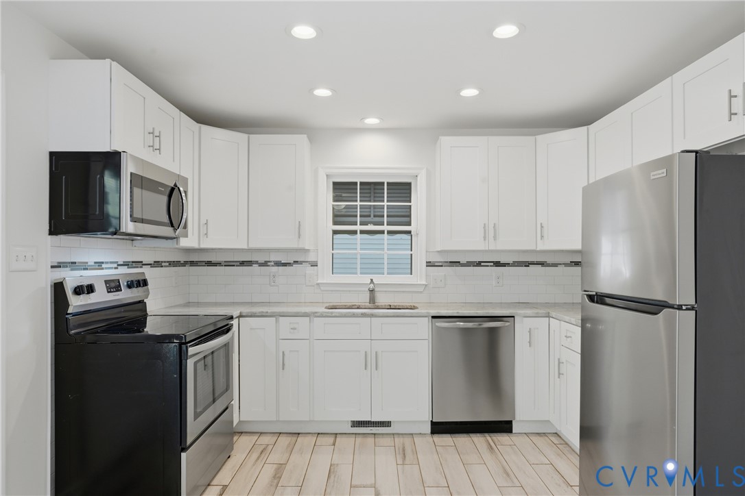 Kitchen featuring white shaker-style cabinetry, stainless steel appliances, tiled backsplash with a decorative accent row, and quartz countertops