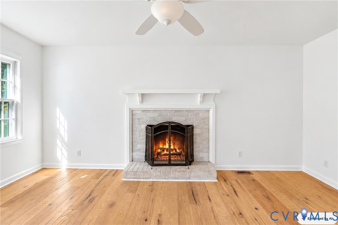 Living area featuring wood-finish flooring, a masonry fireplace with a brick-surround hearth, a traditional mantel, and a ceiling-mounted fan