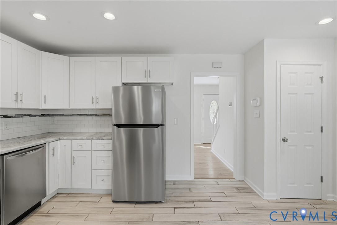 Kitchen featuring white shaker-style cabinetry, stainless steel appliances, light-toned stone-patterned countertops, and a white subway tile backsplash