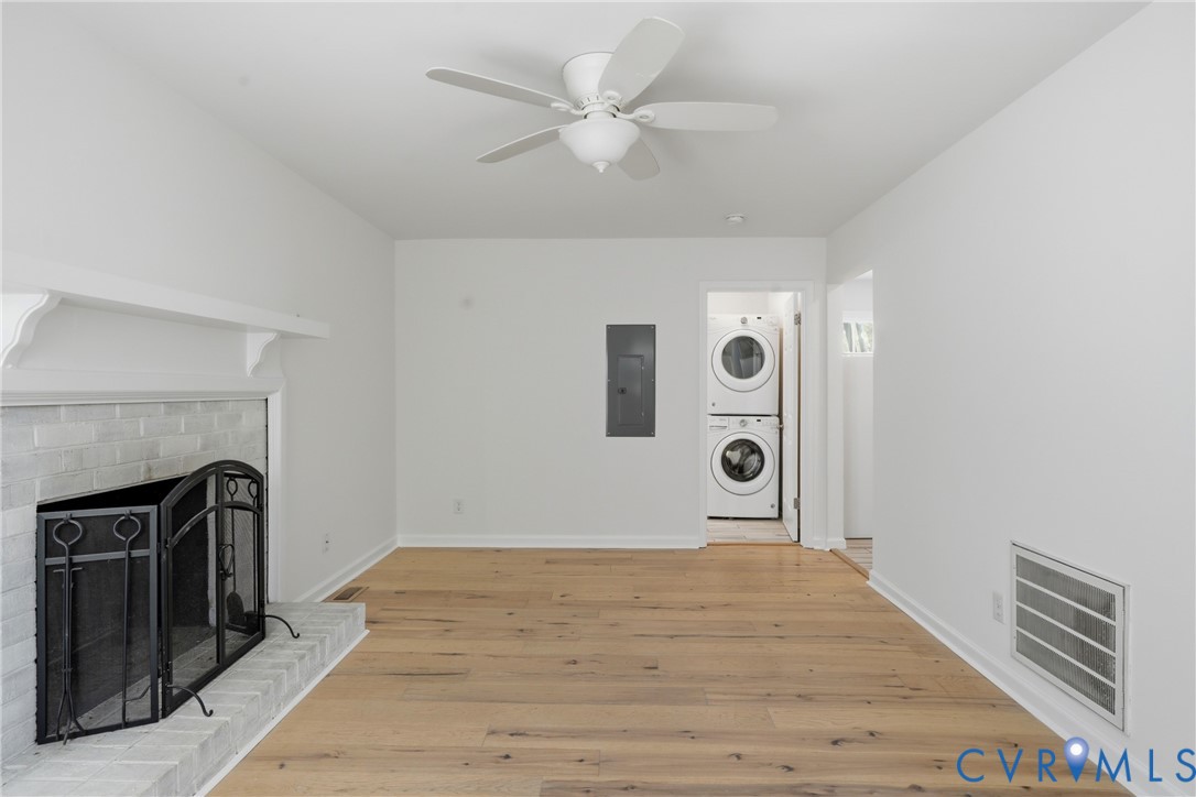 Fireplace with a painted brick surround and mantel, wood-finish flooring, ceiling fan, and built-in stacked laundry appliances