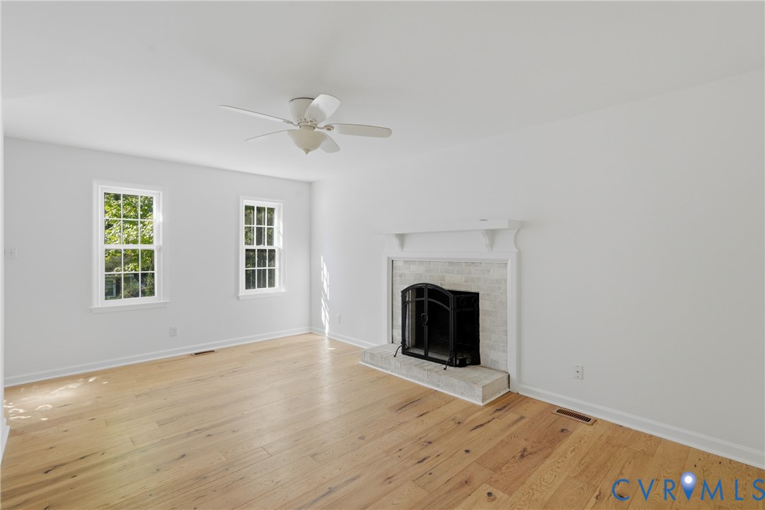 Living area featuring wood-finish flooring, a masonry fireplace with a brick-surround hearth, a traditional mantel, and a ceiling-mounted fan
