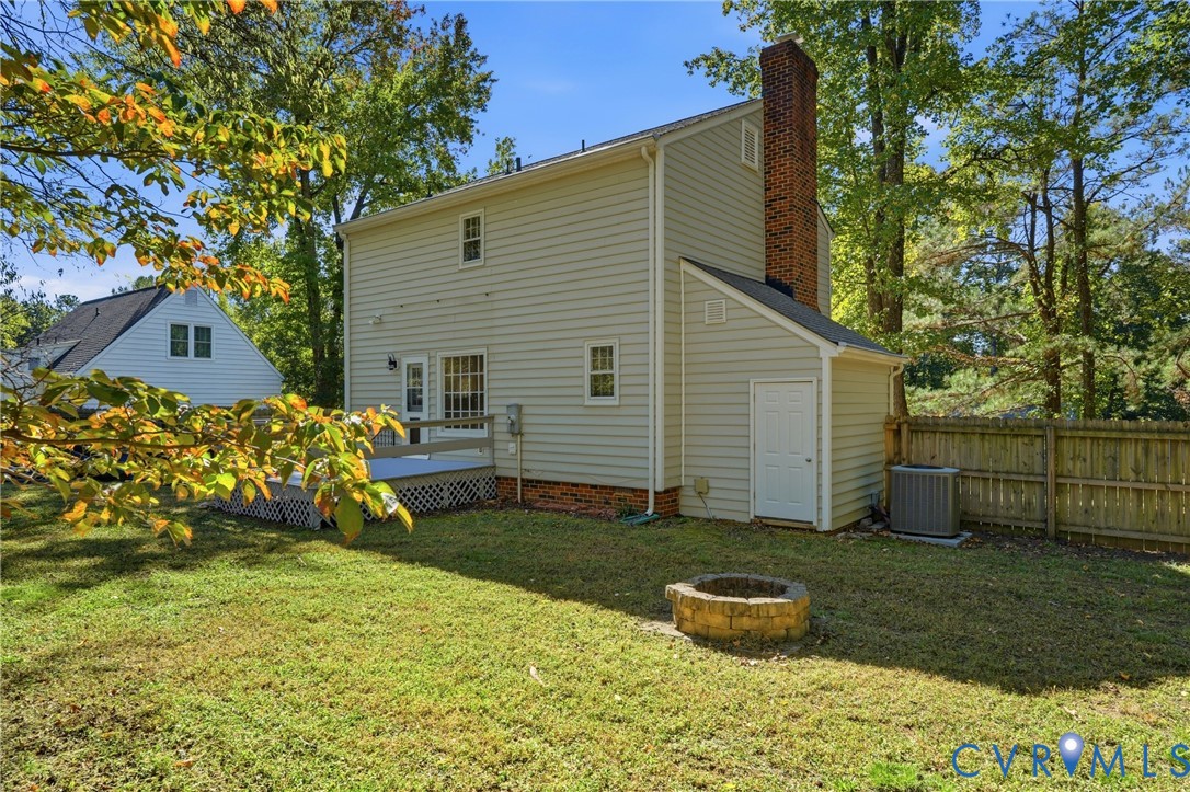 Rear exterior featuring light-toned siding, a brick chimney, a wood-frame deck and a wooden privacy fence