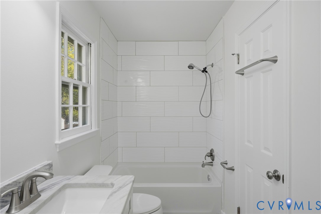 Bathroom featuring a stone-top vanity with an undermount sink, subway tile shower surround, window, and brushed nickel hardware