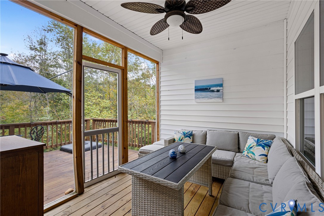 Screened porch featuring wood plank flooring, horizontal white siding, a ceiling fan, and a door leading to a wood deck with railing