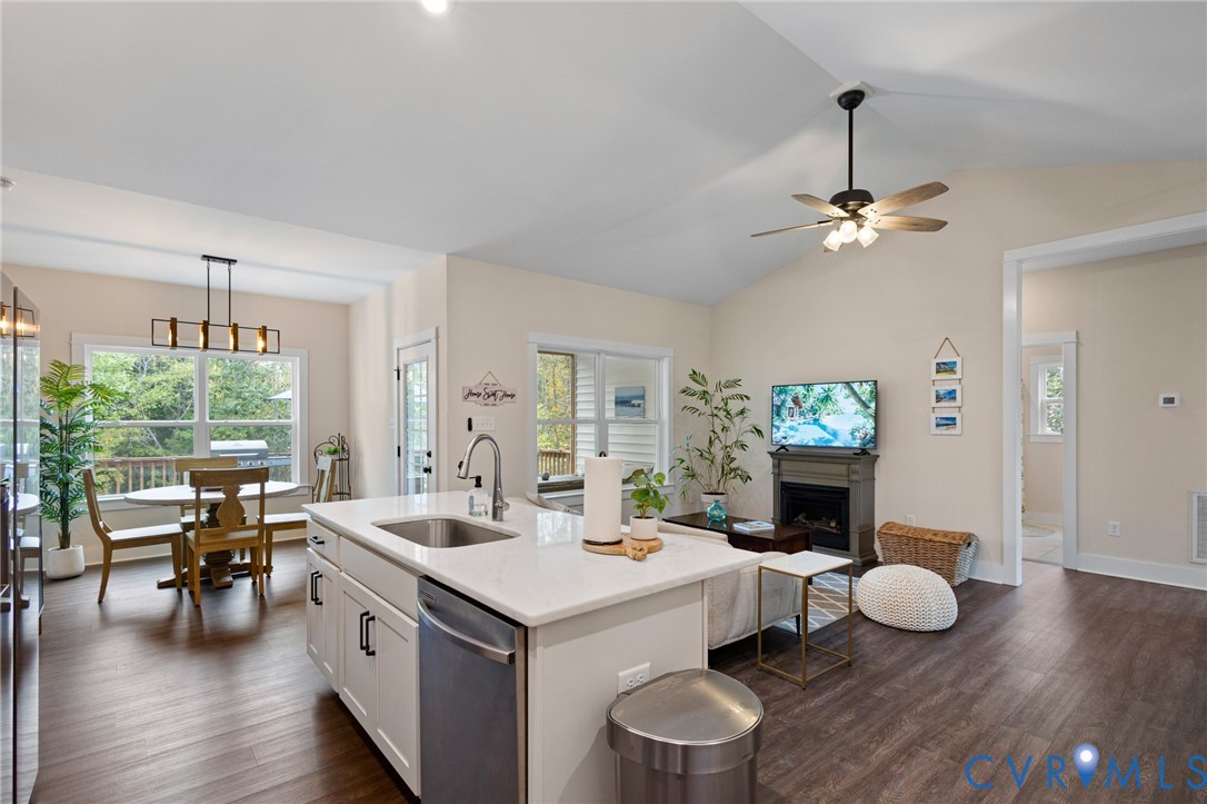 Open-concept interior featuring vaulted ceilings, wood-finish flooring, a central kitchen island with stone-surface countertops, and a built-in fireplace