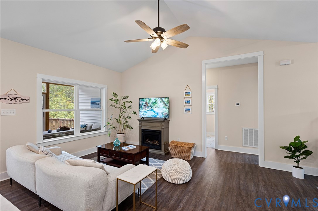 Vaulted ceiling with an integrated multi-blade ceiling fan, wood-finish flooring, and a decorative fireplace mantel