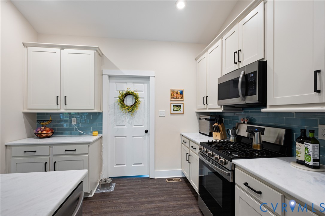 Kitchen featuring shaker-style cabinetry with matte black hardware, stone-composite countertops, blue subway tile backsplash, and dark wood-finish flooring