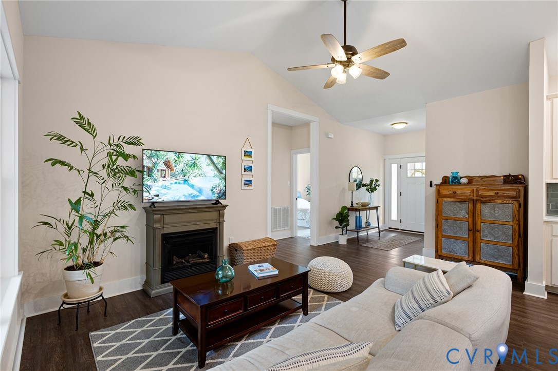 Vaulted ceiling with an integrated multi-blade ceiling fan, wood-finish flooring, and a floor-to-ceiling fireplace mantel