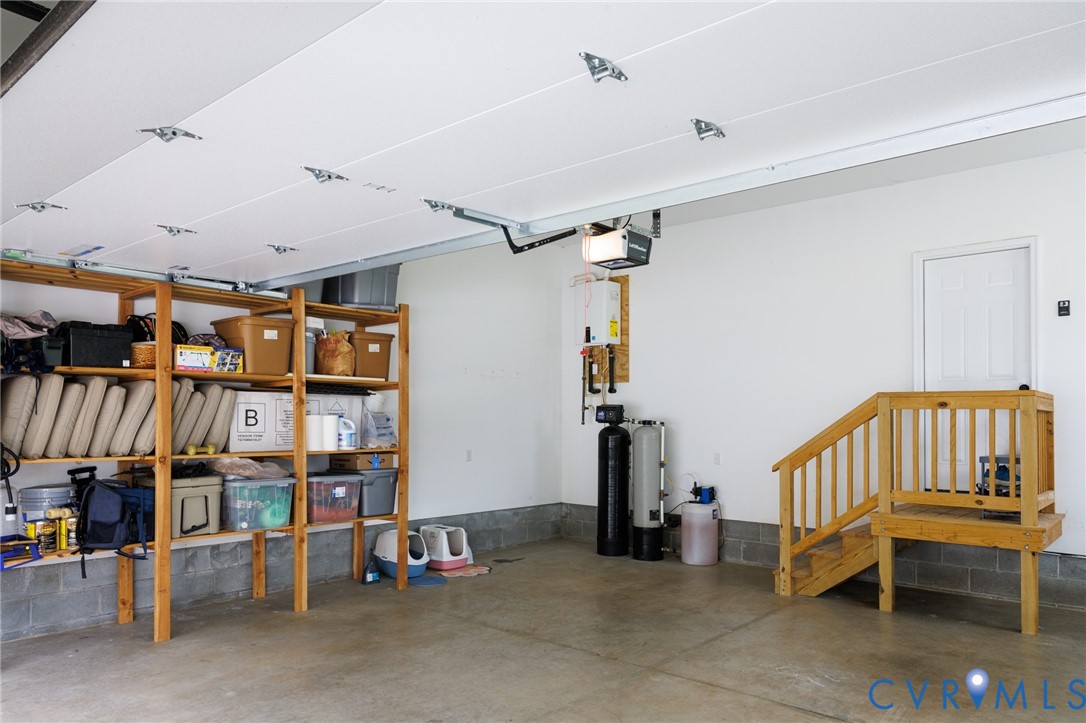 Finished garage space featuring smooth walls, concrete flooring, water treatment system, and wooden staircase with railing