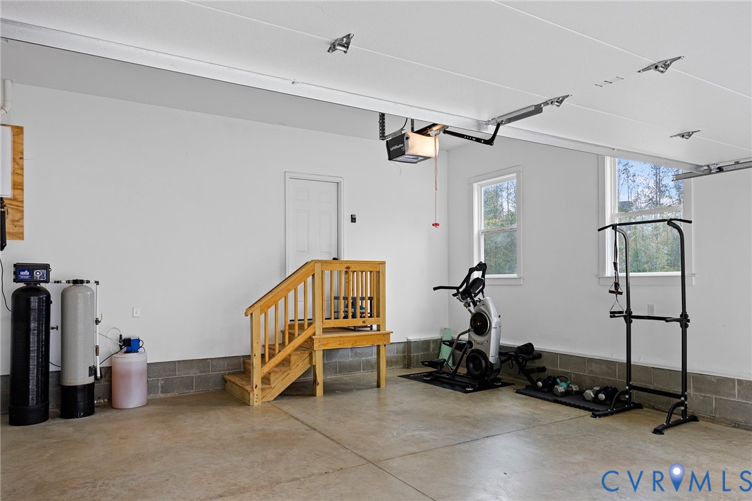 Garage space featuring concrete flooring, painted masonry walls, dual windows, and an integrated water filtration system with a wooden staircase access point