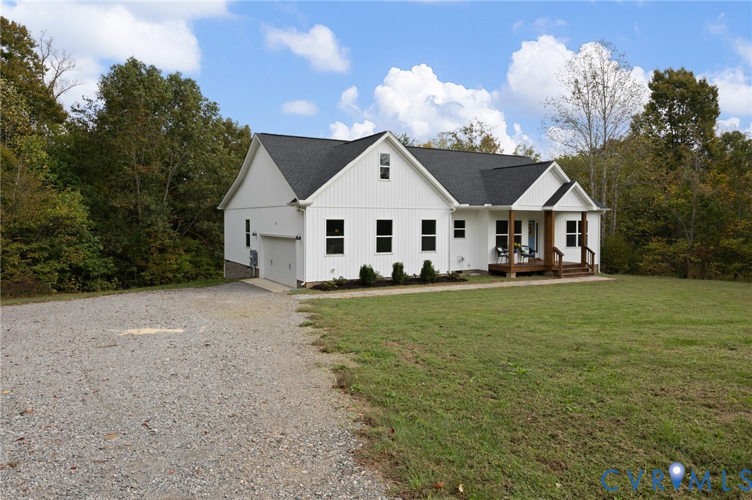 White vertical-siding exterior with a dark shingle roof, covered front porch, and attached garage on a large cleared lot