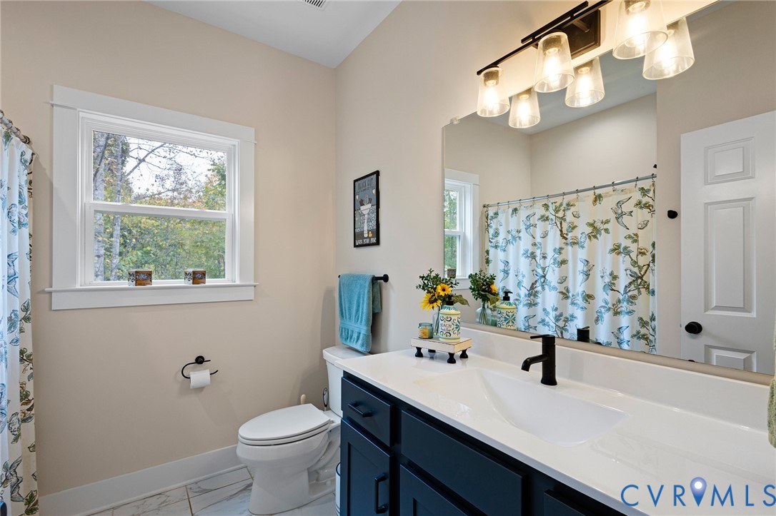 Bathroom featuring a vanity with dark cabinetry and a white countertop, an integrated basin, a matte black faucet, and a large-format vanity mirror with integrated four-bulb lighting