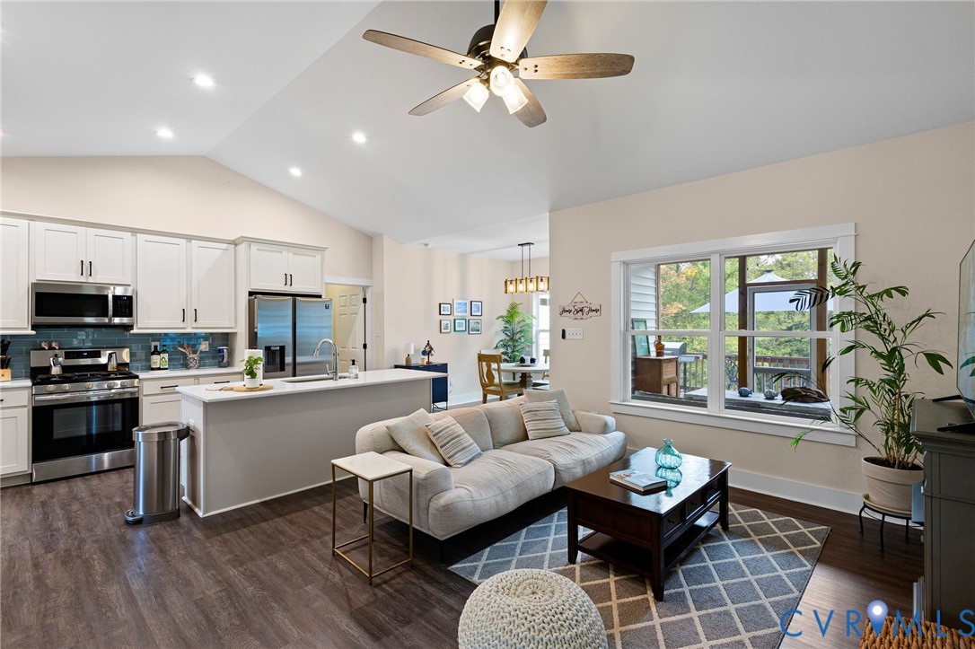 Vaulted ceiling, white shaker-style cabinetry, stainless steel appliances, kitchen island, and wood-finish flooring