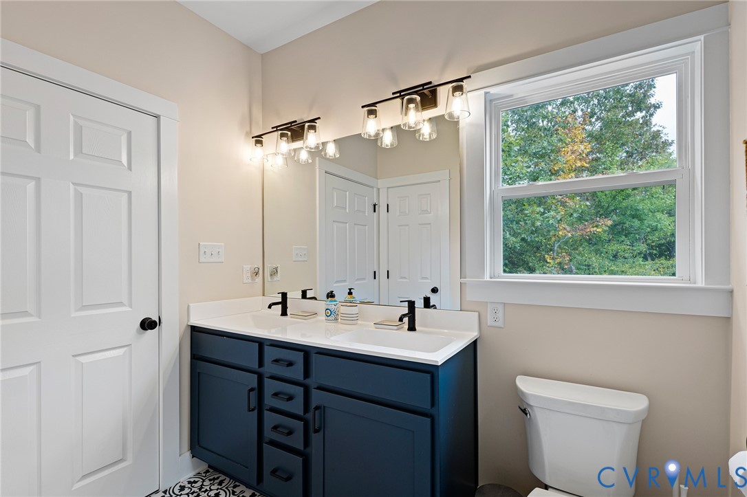 Dark blue dual-sink vanity with a white countertop, two matte black faucets, oversized wall mirror, and two multi-light fixtures