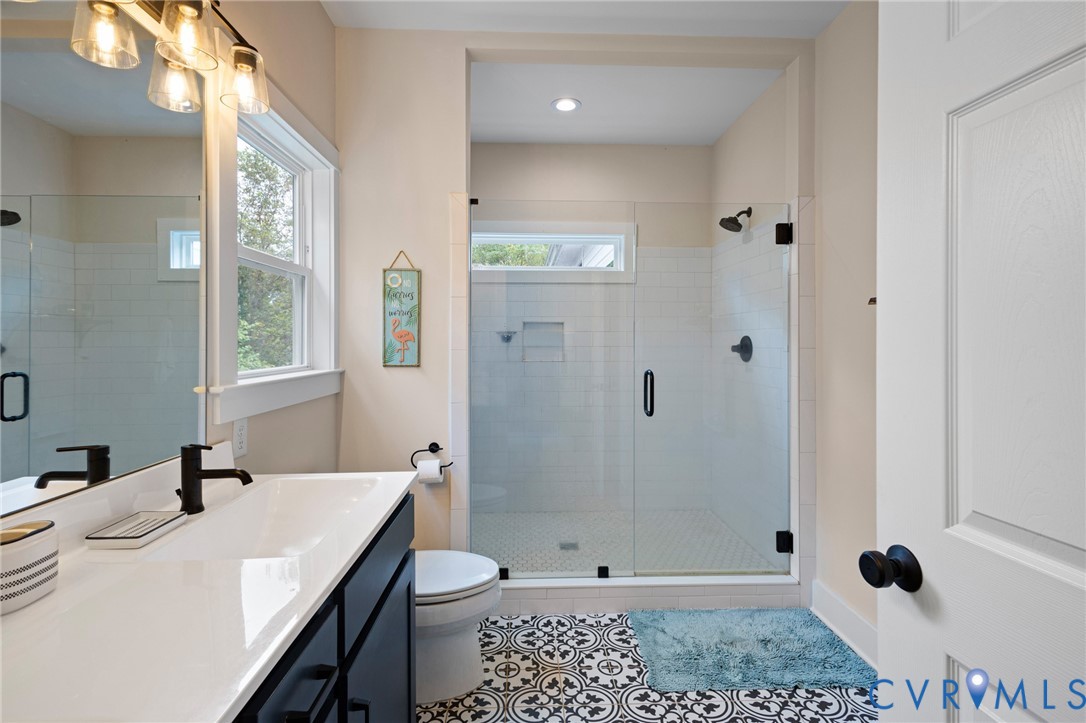 Bathroom featuring a dark vanity with a white countertop, patterned tile flooring, a glass-enclosed shower with subway tile surround, and matte black hardware