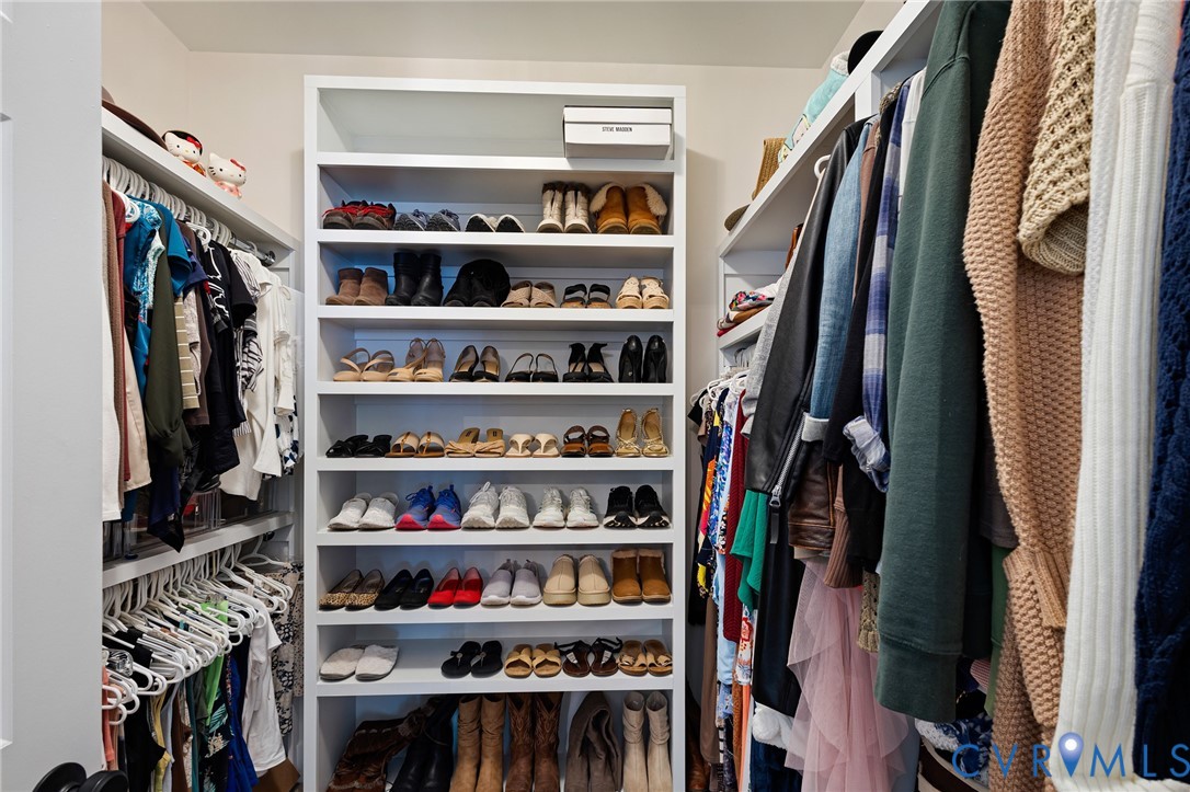 Walk-in closet featuring custom white built-in shelving and integrated garment rods