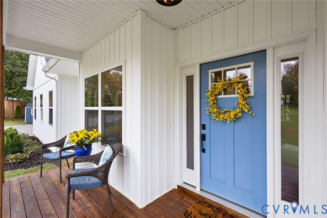 Covered front porch with wood-finish decking, vertical board siding, blue entry door with a window insert, and sidelight windows