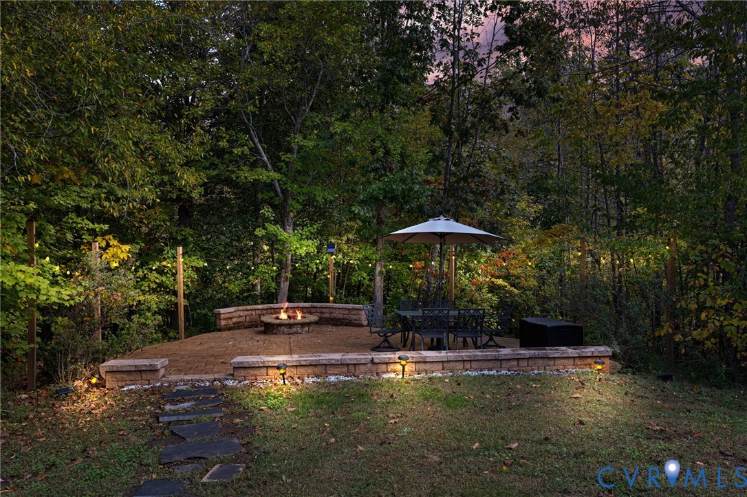 Tiered stone patio featuring a built-in fire pit, stone retaining walls, slate pathway, and string lighting