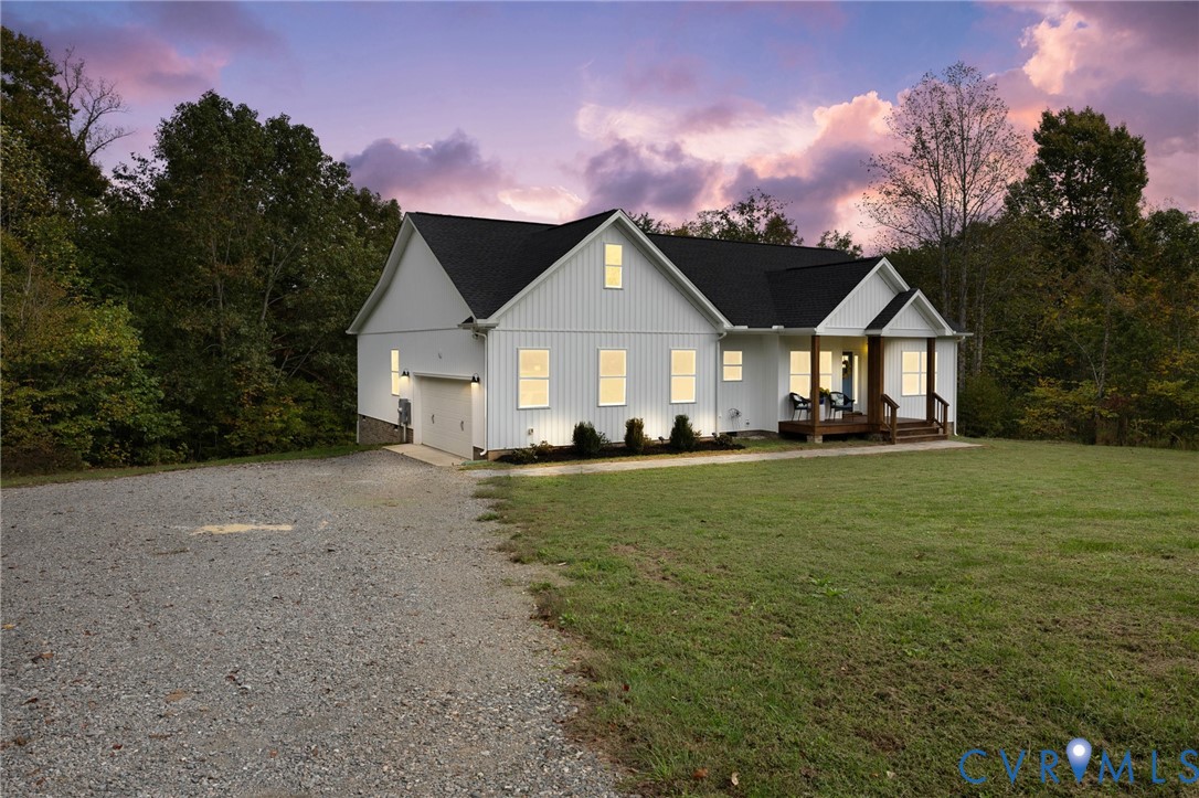 Modern farmhouse exterior featuring vertical board-and-batten siding, a covered front porch, an attached garage, and a gravel driveway