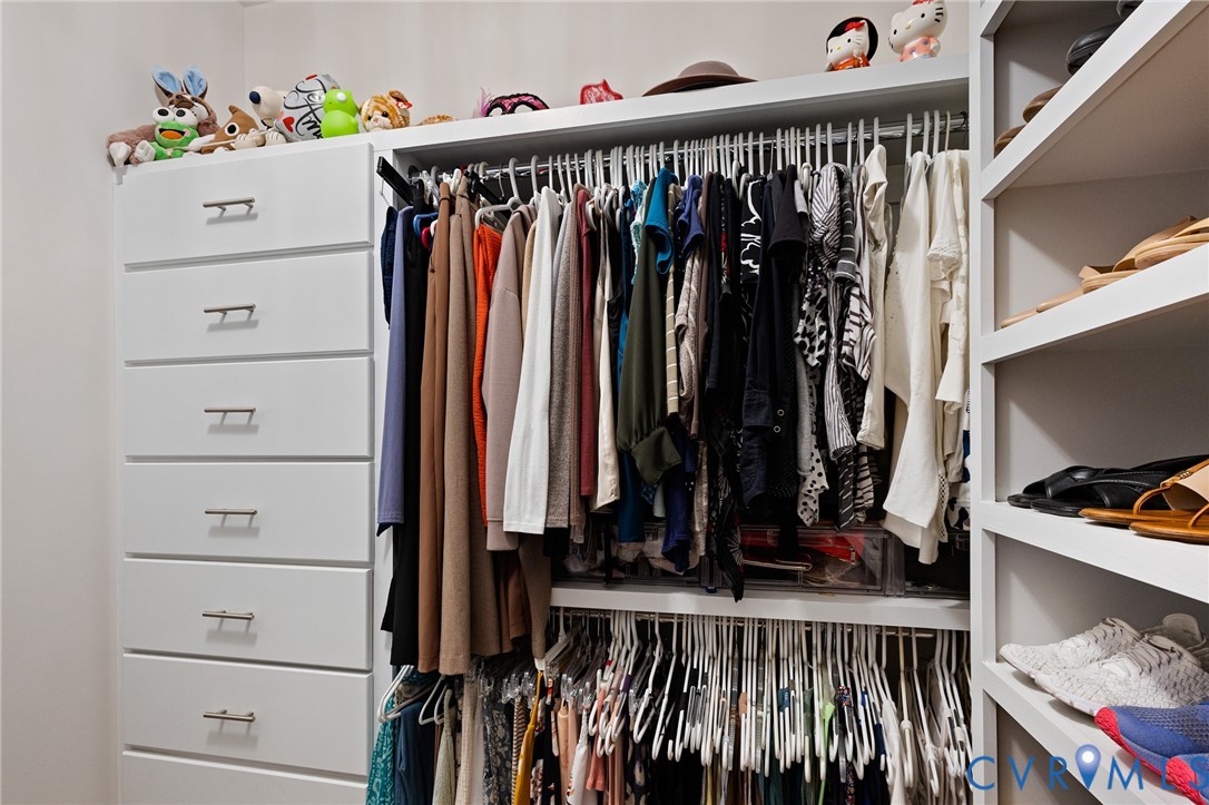 Walk-in closet featuring white built-in cabinetry, floor-to-ceiling shelving, stainless steel hardware, and dual-level garment rods