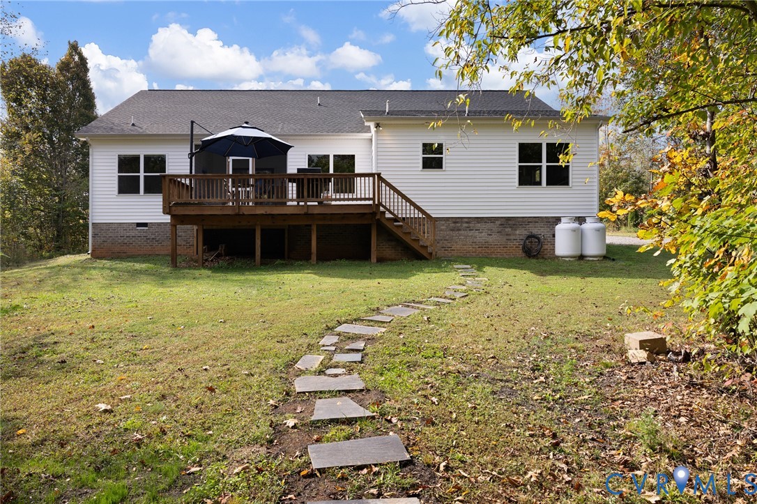 Exterior rear elevation featuring white siding, a brick foundation, an elevated wooden deck with railings, and a flagstone path