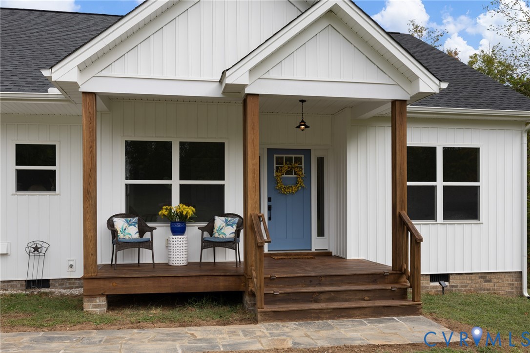 White board-and-batten siding exterior featuring a covered front porch with wood-finish decking, natural timber support posts, and a stone-paver walkway