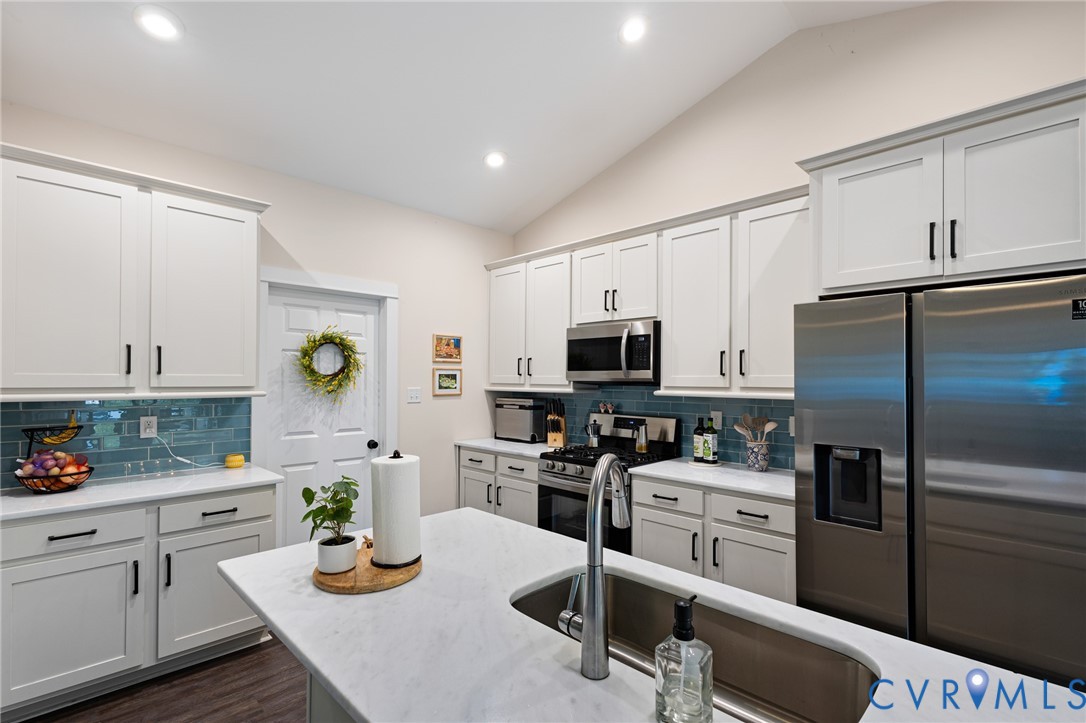 Kitchen featuring white shaker-style cabinetry, a central island with a solid-surface countertop, stainless steel appliances, blue tile backsplash, and recessed lighting