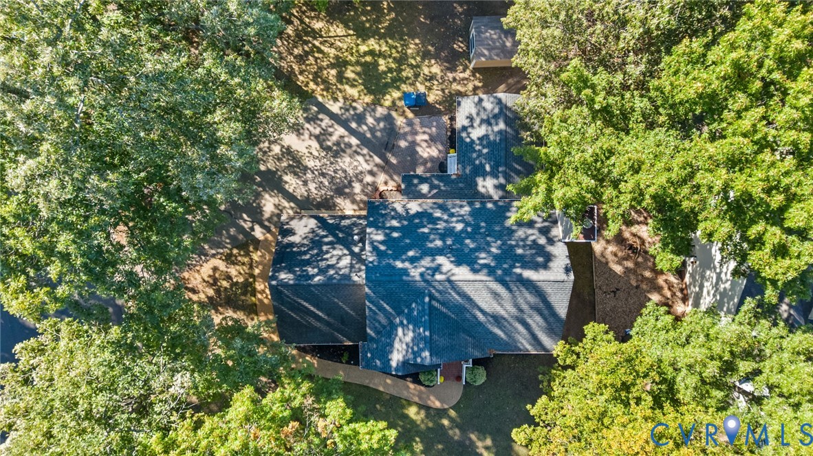 Aerial perspective of property featuring a shingled roof, paved driveway, brick-bordered walkway, and mature trees across a spacious lot