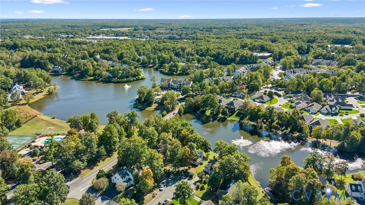 Aerial perspective of a multi-acre community featuring expansive water elements, dual decorative fountains, abundant mature tree canopy, and paved roadway infrastructure